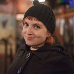 A young red haired woman in a black beanie and a black sweater.